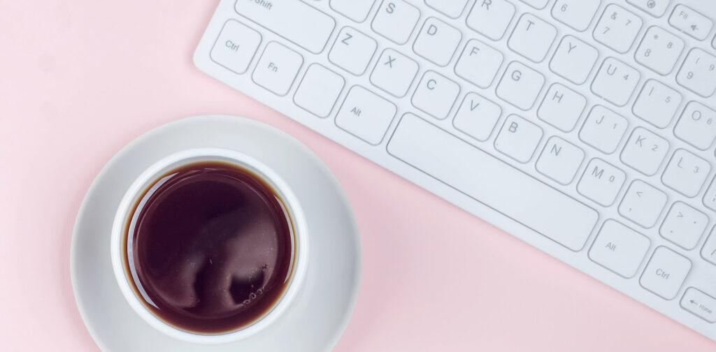 Cup of coffee and computer keyboard on a pink background