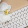 computer keyboard with white orchid flower on beige background